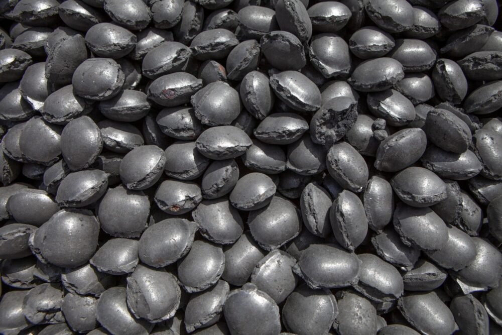 Close-up view of piled iron briquette pellets, showcasing their dense, metallic texture and compact granular form.