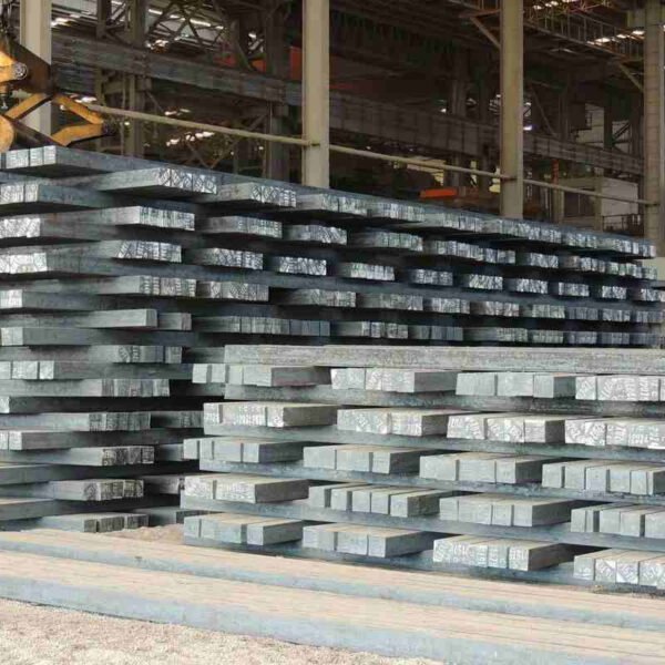 Large rectangular steel blooms stacked on a factory floor, ready for further processing.