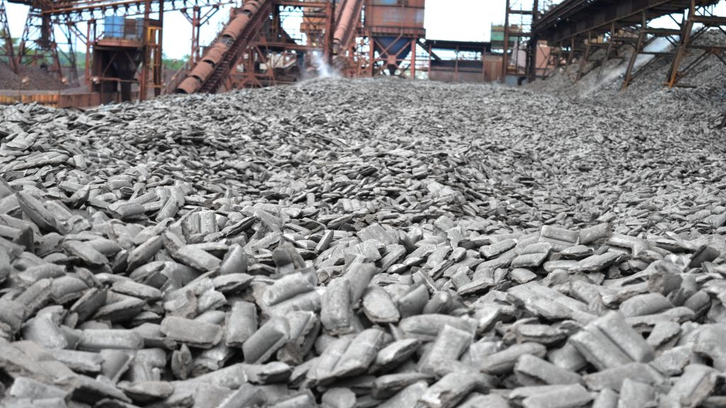 close up of a pile of hot briquetted iron with machines visible in the distance
